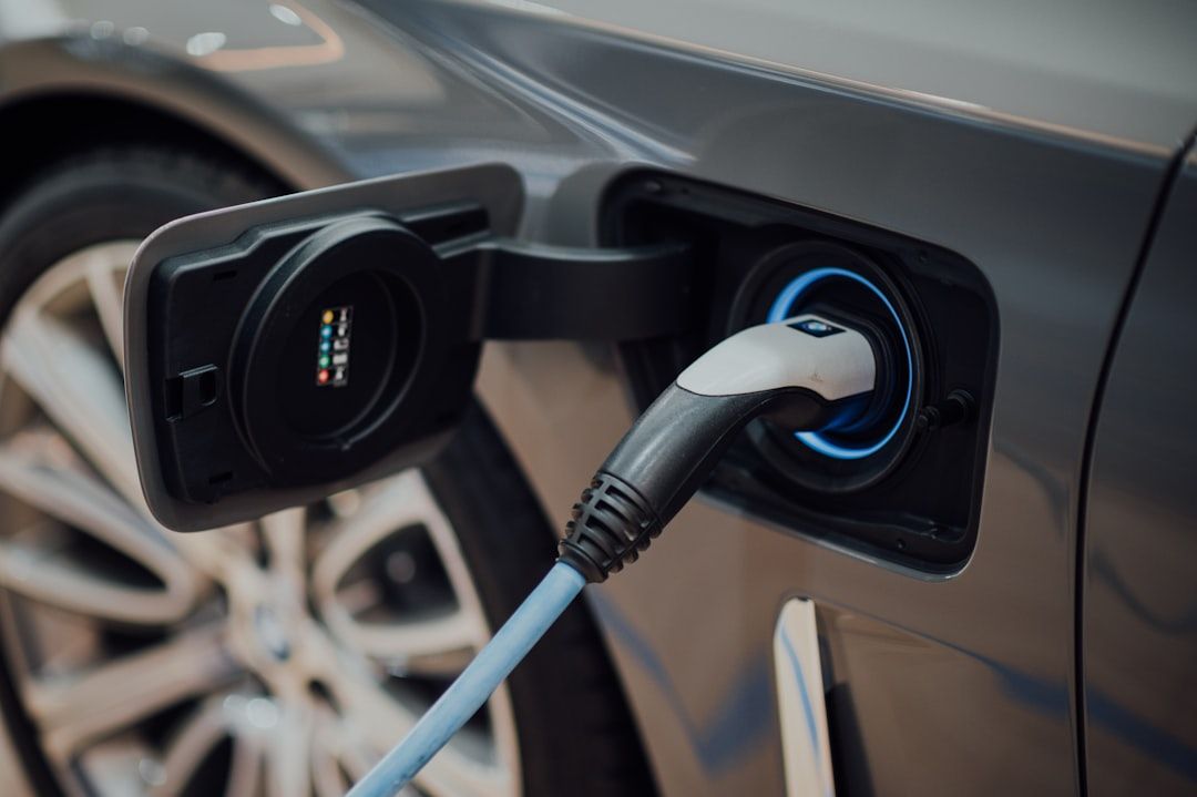 Harmaa sähköauto latauksessa latausasemalla julkisella paikalla.